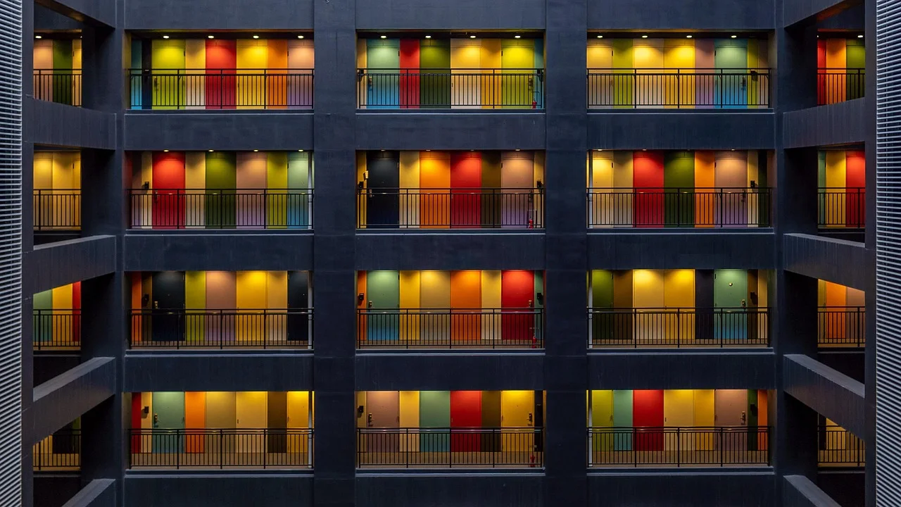 Façade intérieure d’un immeuble aux portes colorées, réparties sur plusieurs étages.